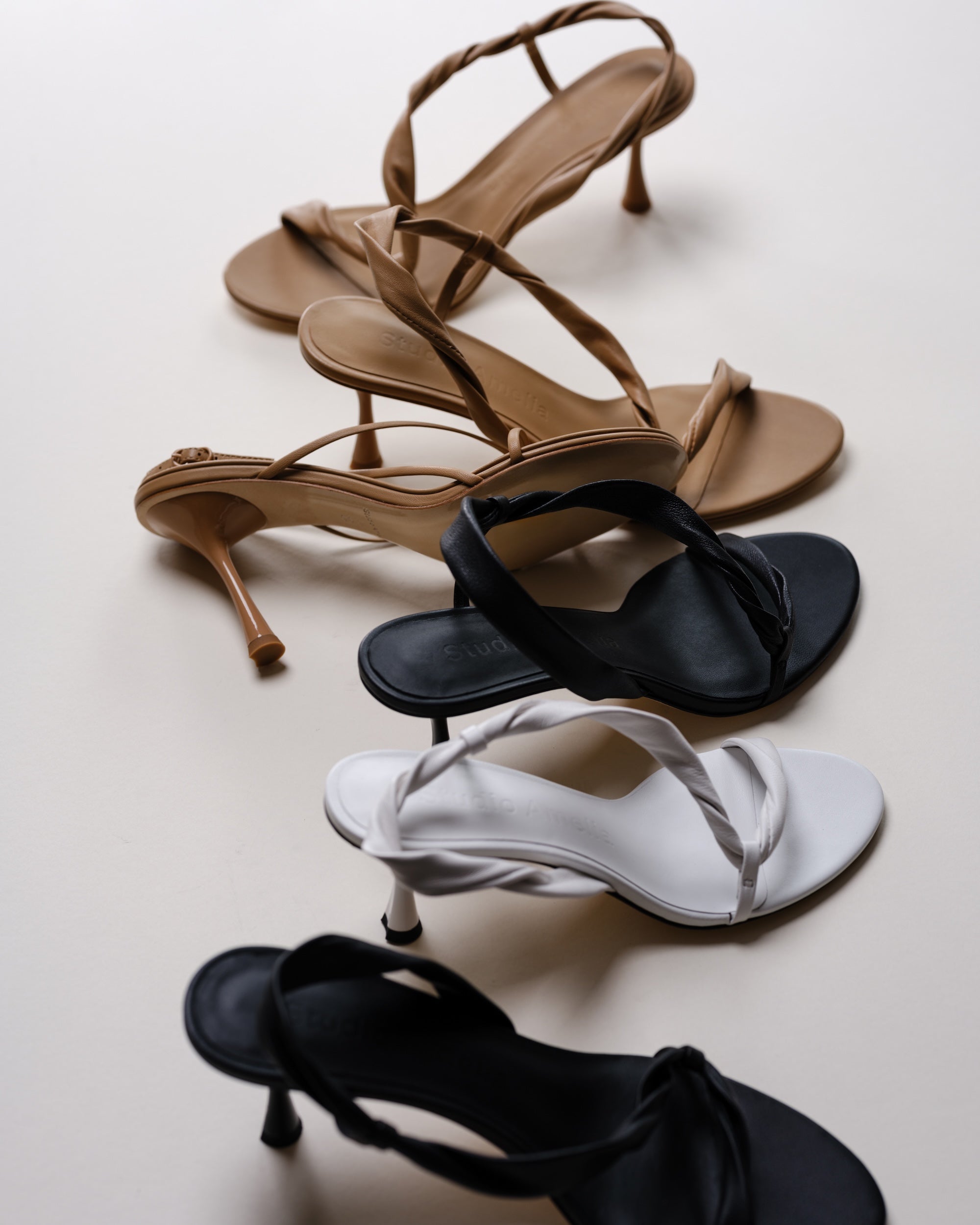 Set of high-heeled sandals in brown, black, and white on a light background