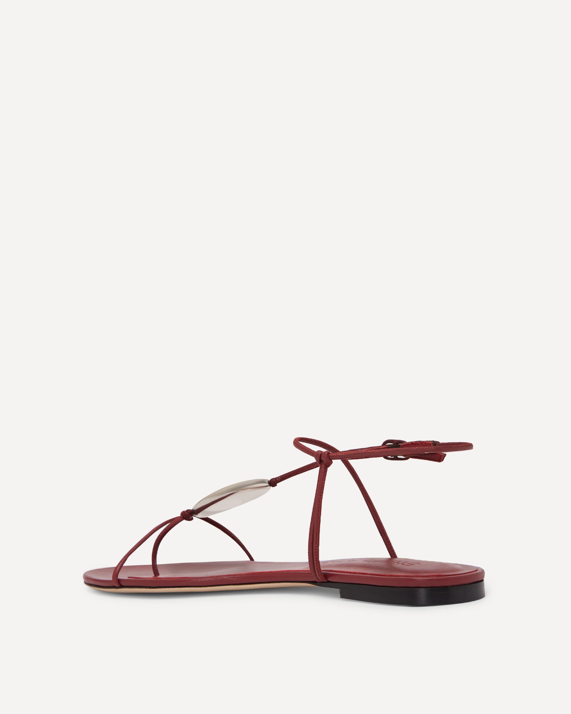 Maroon coloured flat sandals with thin straps on a white background