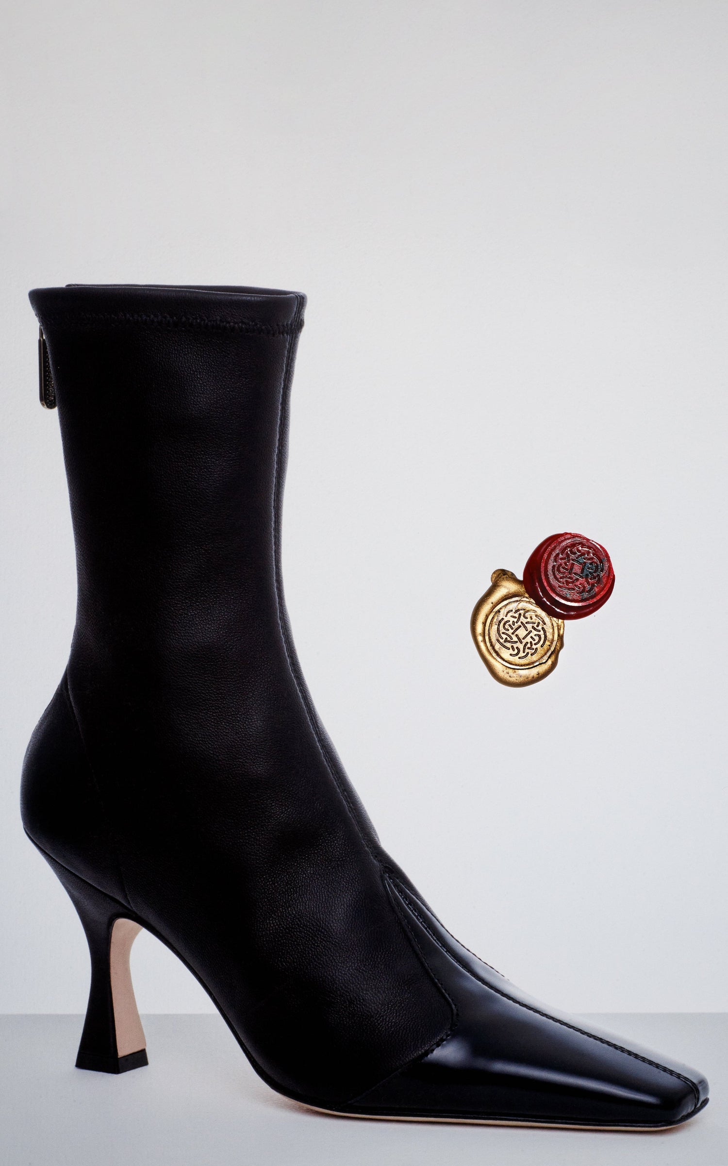 Black high-heeled boot on a light gray background with two decorative seals.