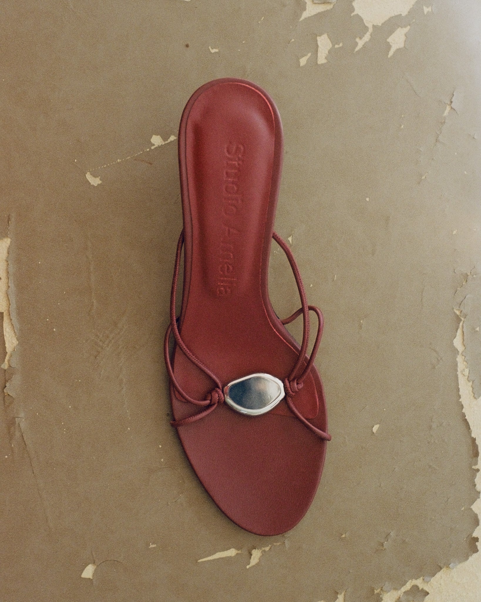 Red sandal with a silver charm on a textured brown background