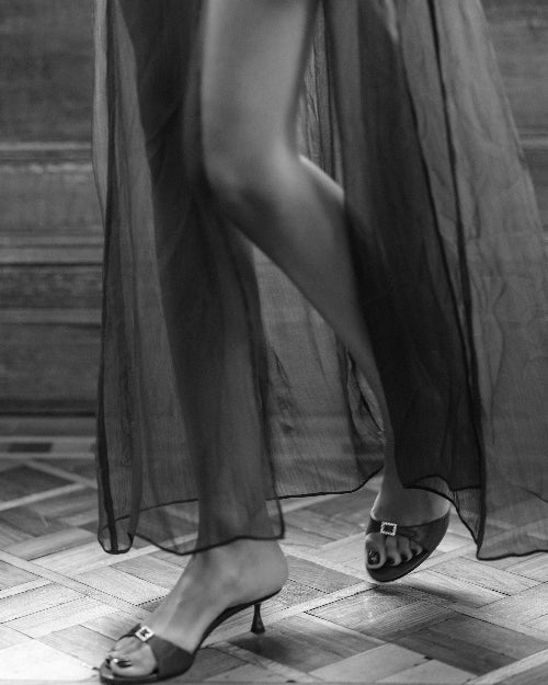 A woman wearing open toe kitten heel sandals with silver buckle