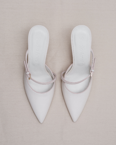 Pair of white pointed-toe shoes with thin straps on a beige background