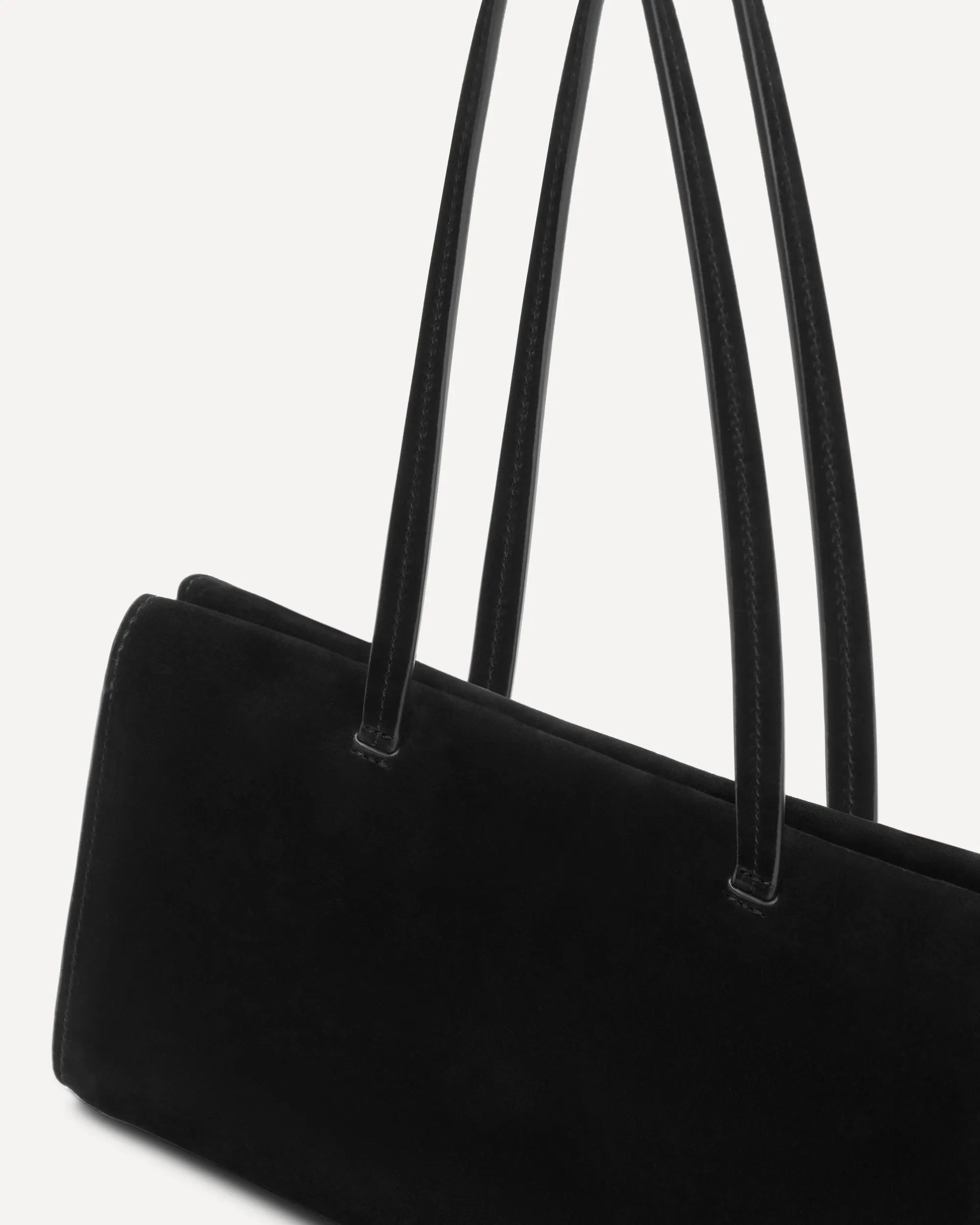 Close-up of a black tote bag with long shoulder straps, shown against a plain light background.