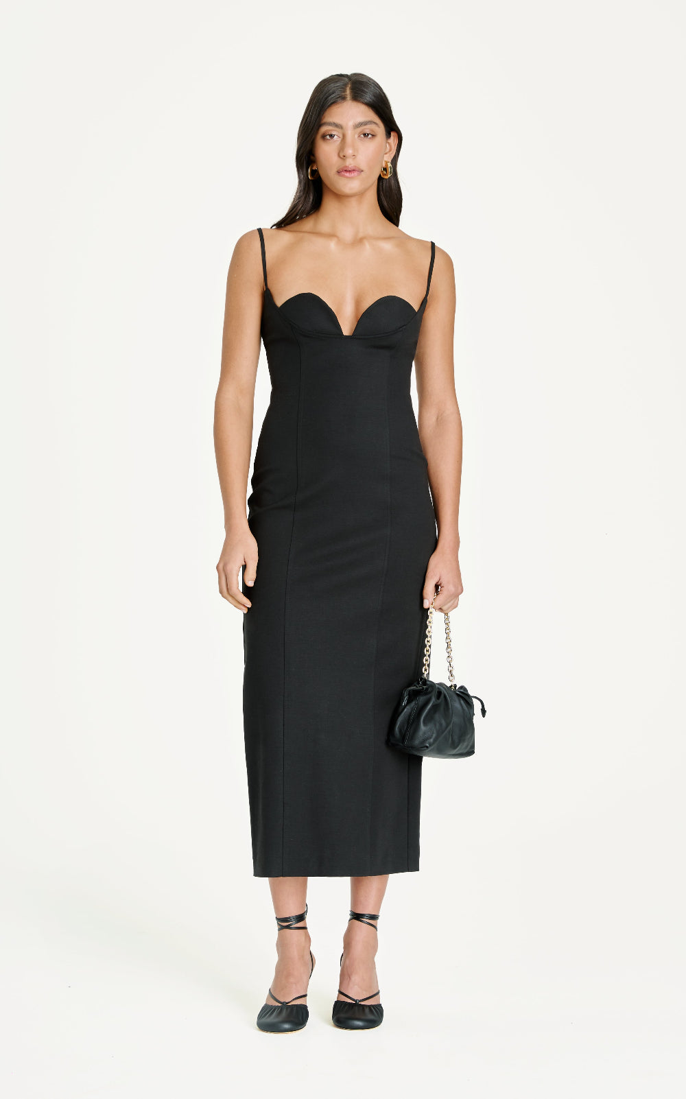 Woman wearing a black slip dress holding a matching handbag on a white background
