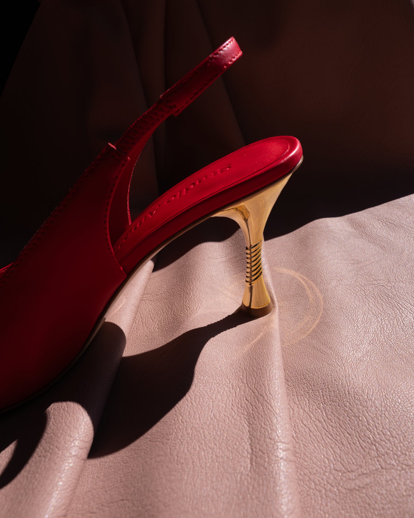 Red high-heeled shoe with a gold heel on a pink surface