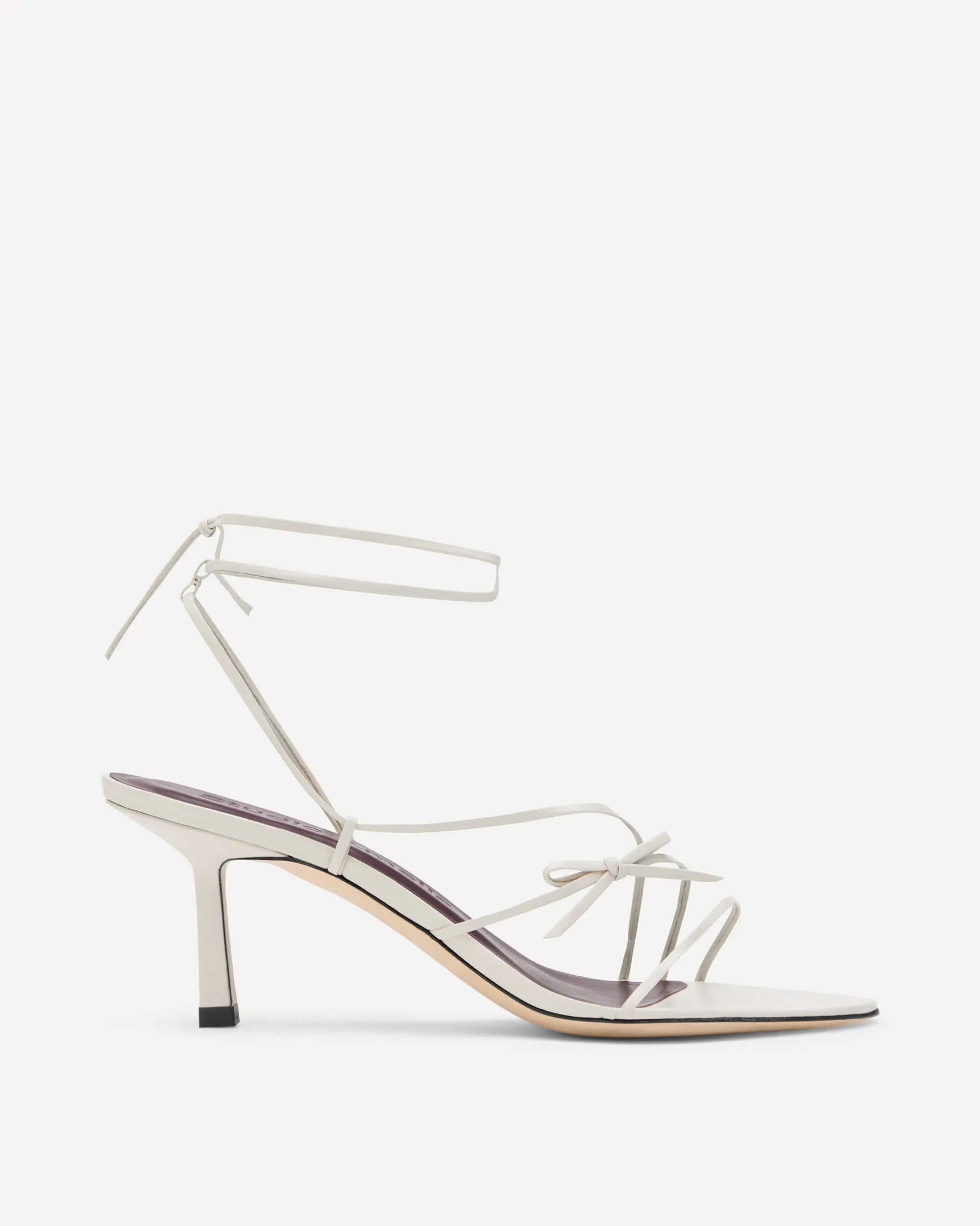 A single white leather high-heeled sandal with thin wraparound ankle straps, a pointed toe, and a stiletto heel, shown from a side profile on a light off-white background.