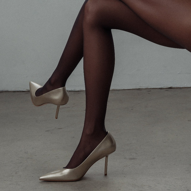 Gold high-heeled shoes worn with dark tights against a neutral background