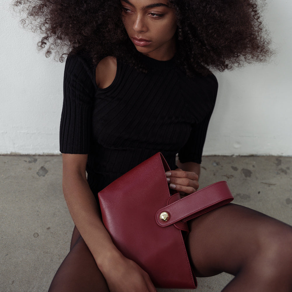 Woman holding a red clutch bag against a neutral background
