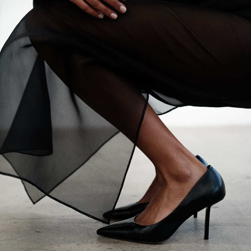 Person wearing black high-heeled shoes with a flowing black skirt on a light background