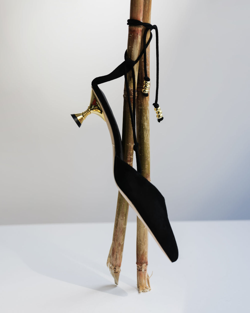 Black kitten heeled shoe with gold accents hanging on a bamboo stick