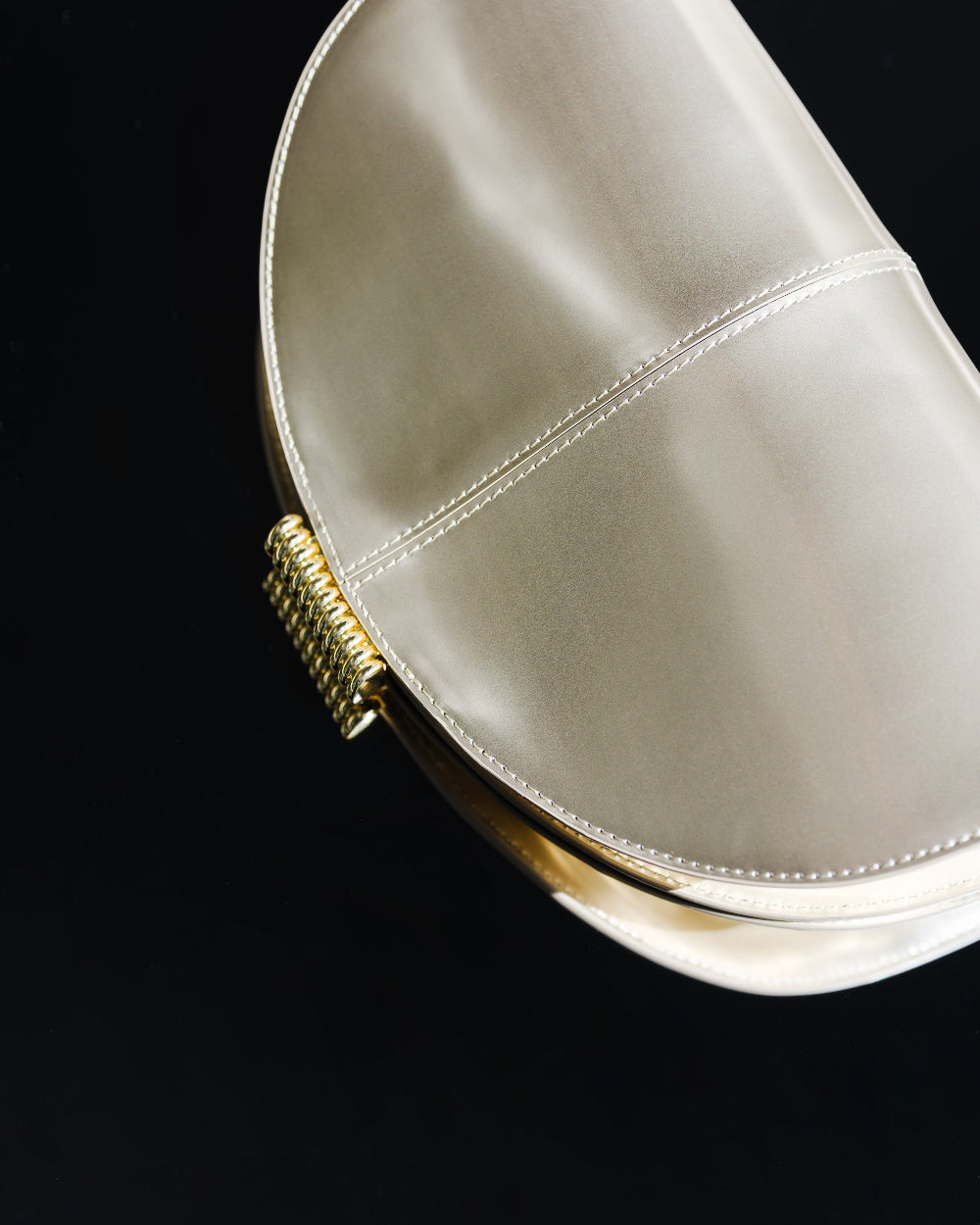A gold handbag with gold clasp on a black background