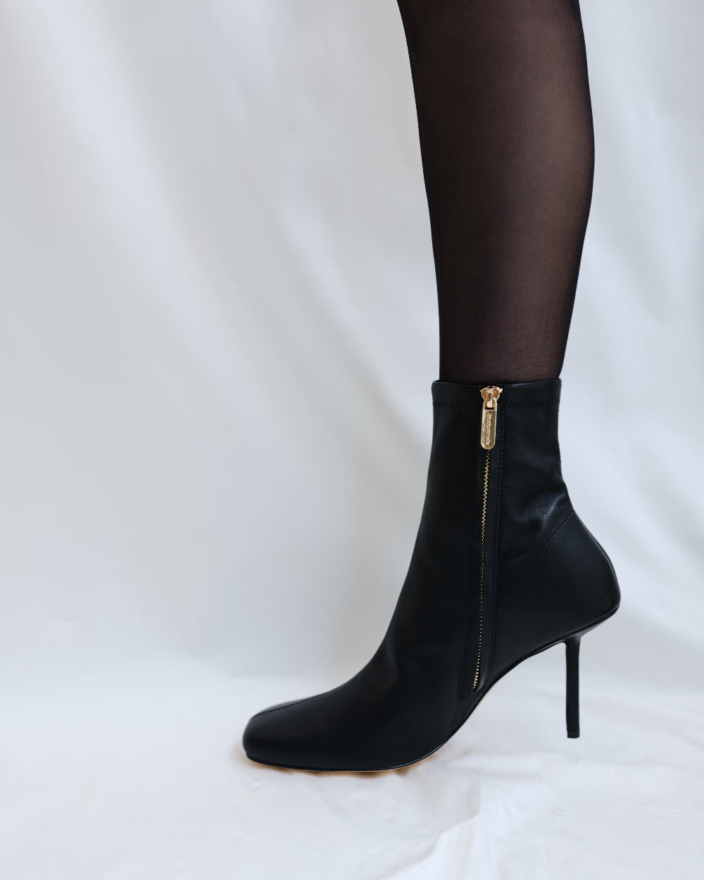 Black ankle boot with a gold zipper on a white background