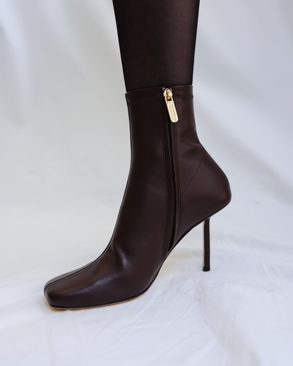 A brown leather boot with high heels and gold zipper