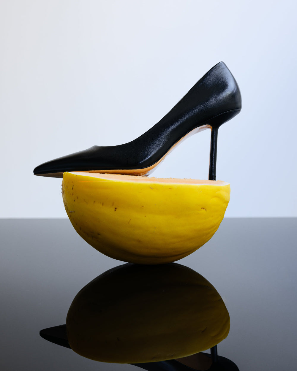 Black leather high heels sitting on a fruit