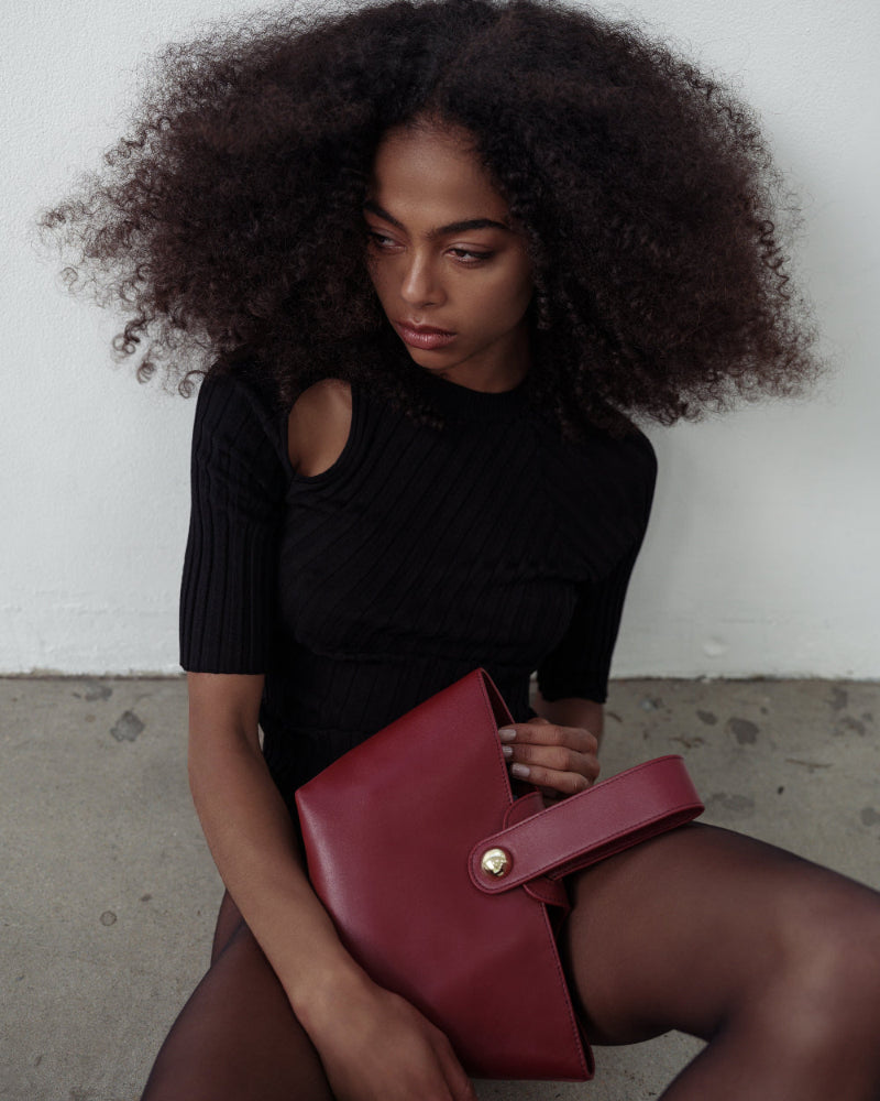 Woman holding a red clutch bag against a neutral background