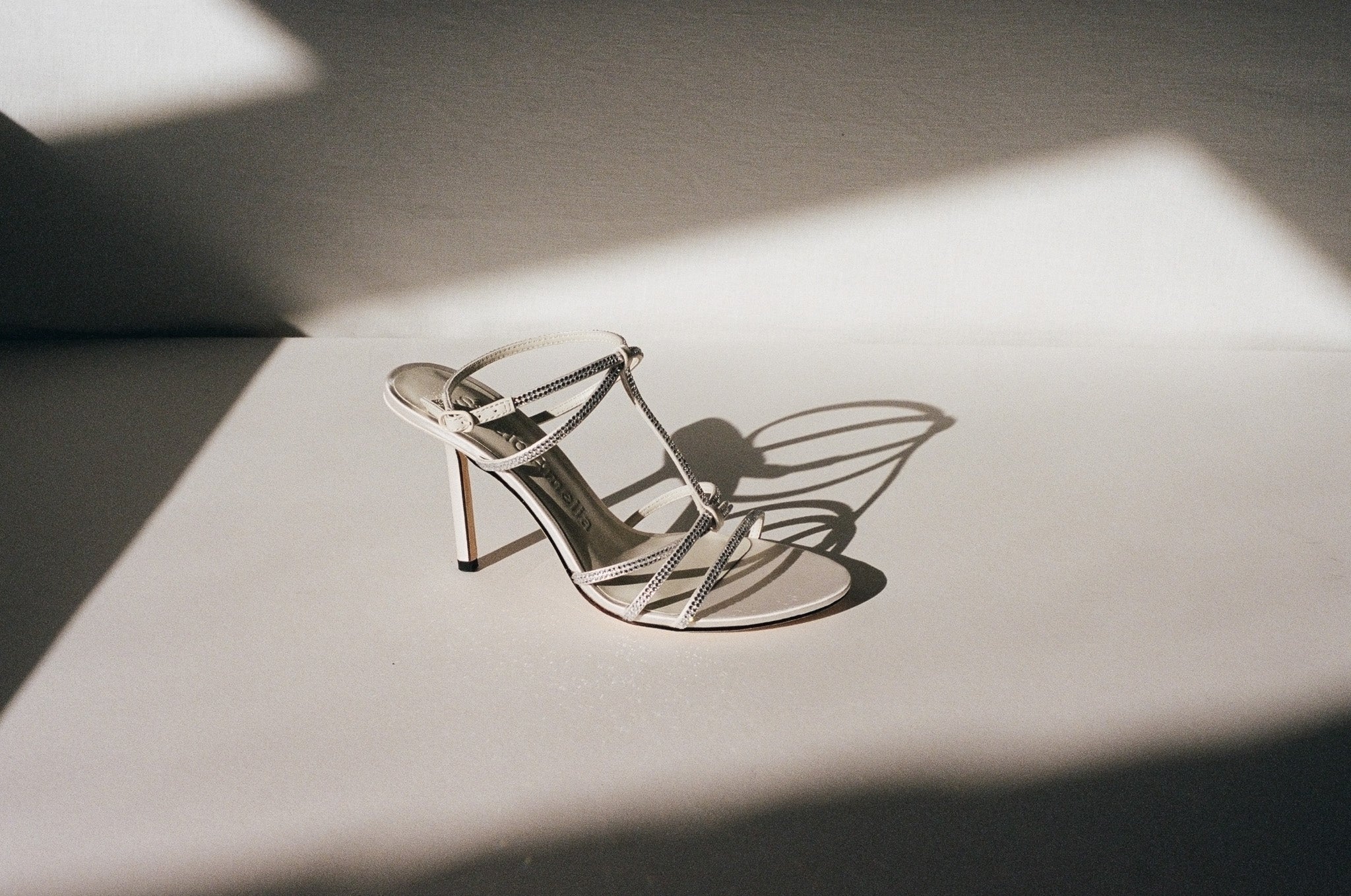 Silver high-heeled shoe on a reflective surface with shadows
