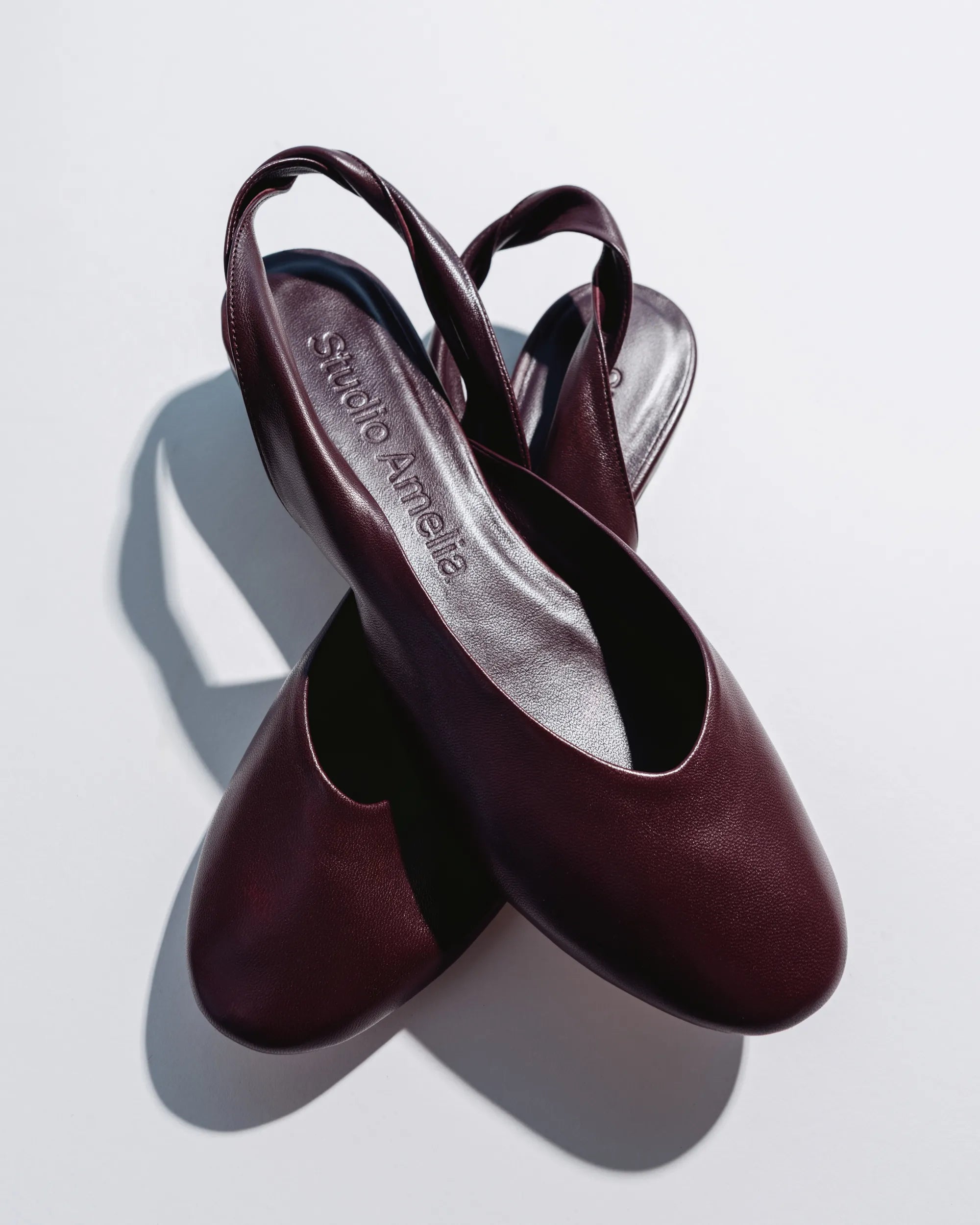 A pair of dark burgundy leather slingback pumps with low block heels, displayed on a clean white background with a soft shadow.