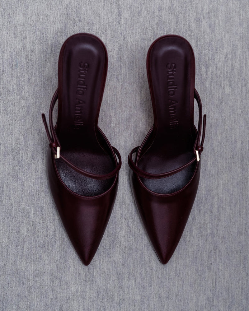 Pair of dark red pointed-toe shoes on a gray background