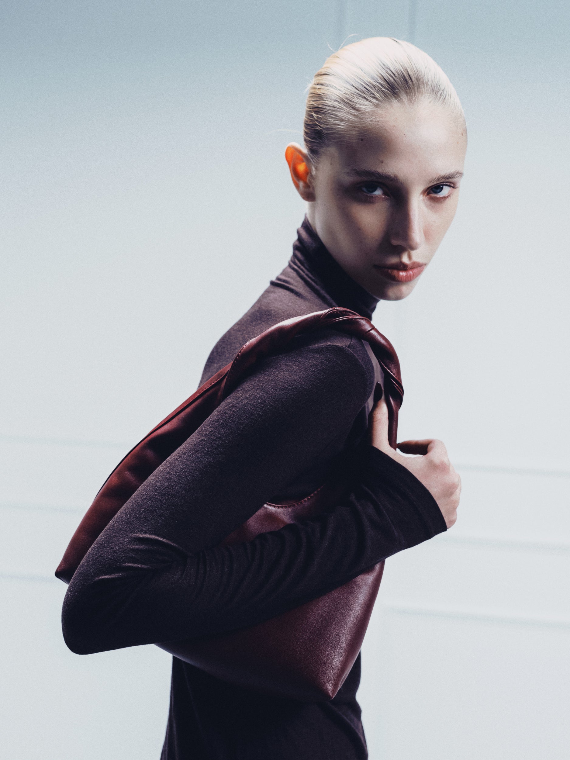 A woman wearing a burgundy leather handbag or shoulder bag made by Studio Amelia