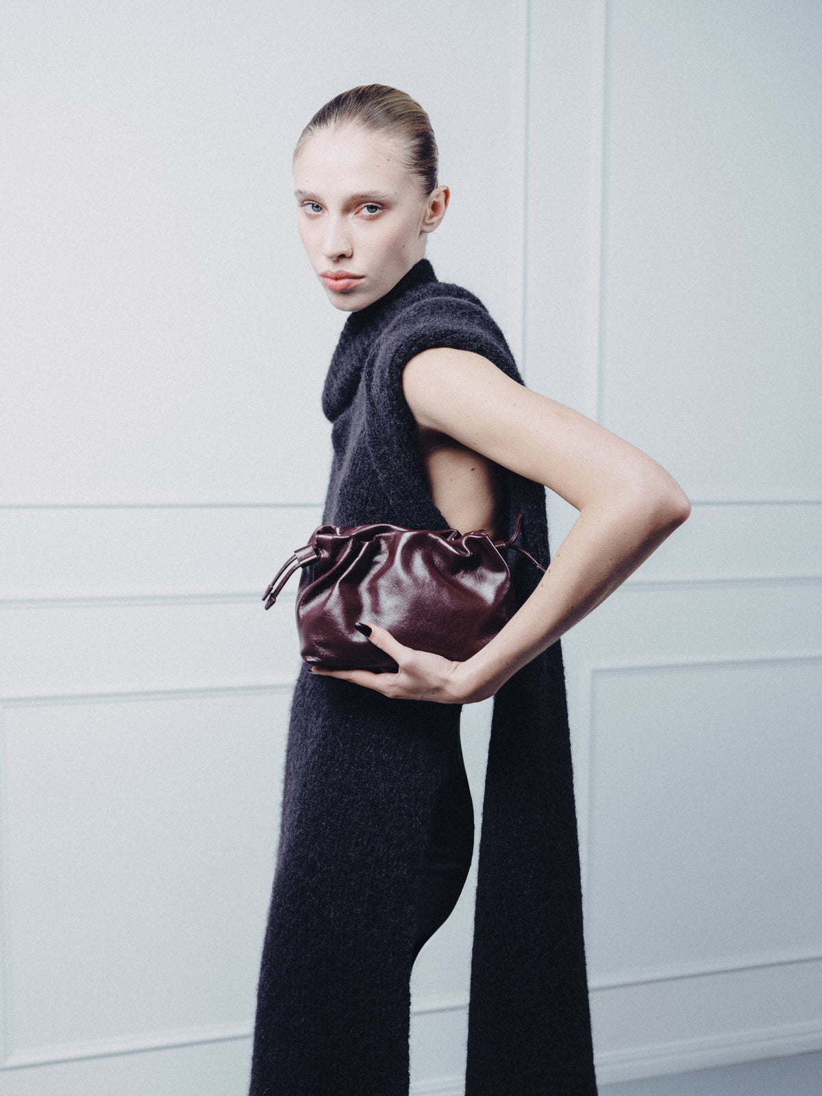 A woman holding a burgundy leather clutch handbag