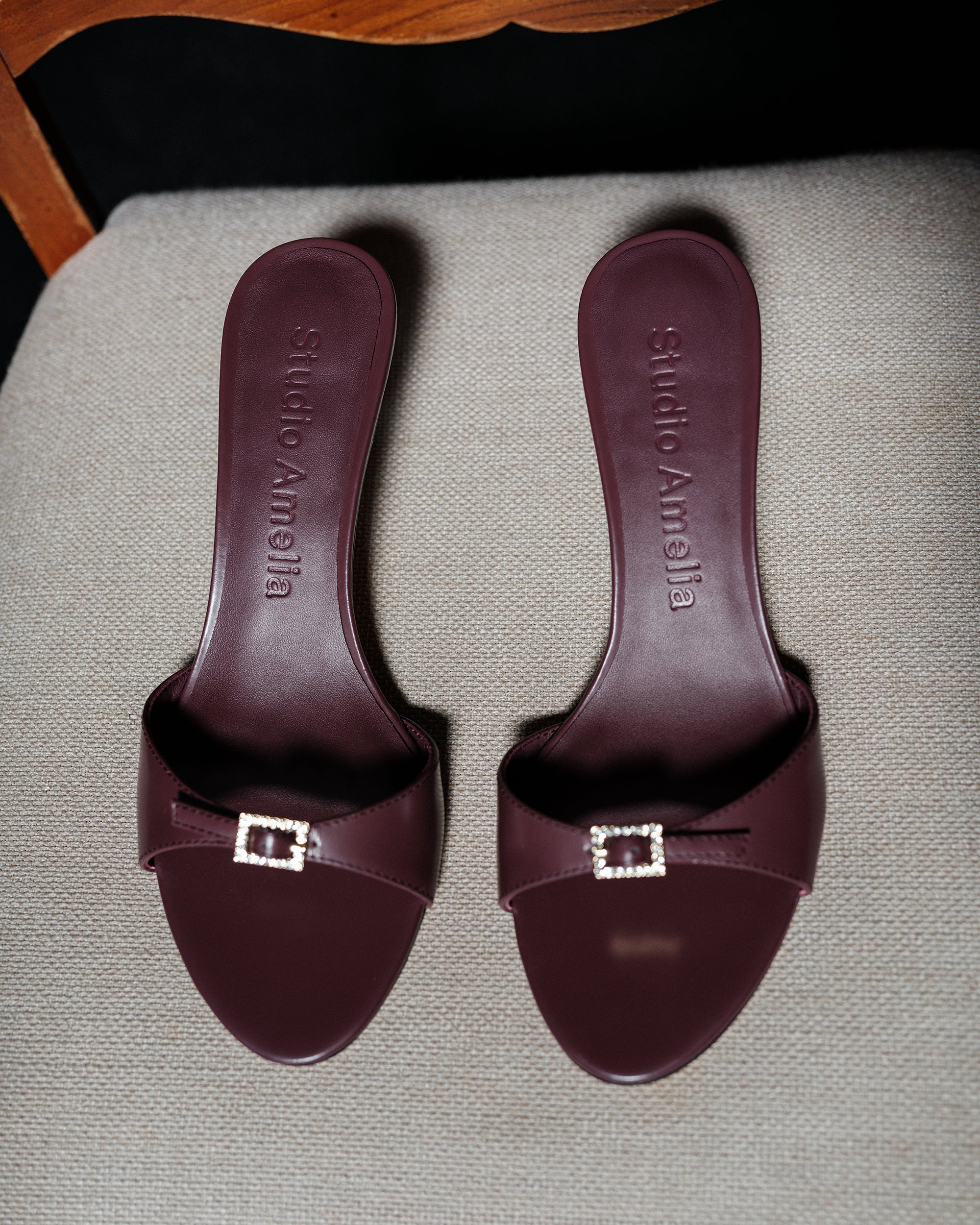 A pair of maroon sandals with 'Studio Amelia' logo