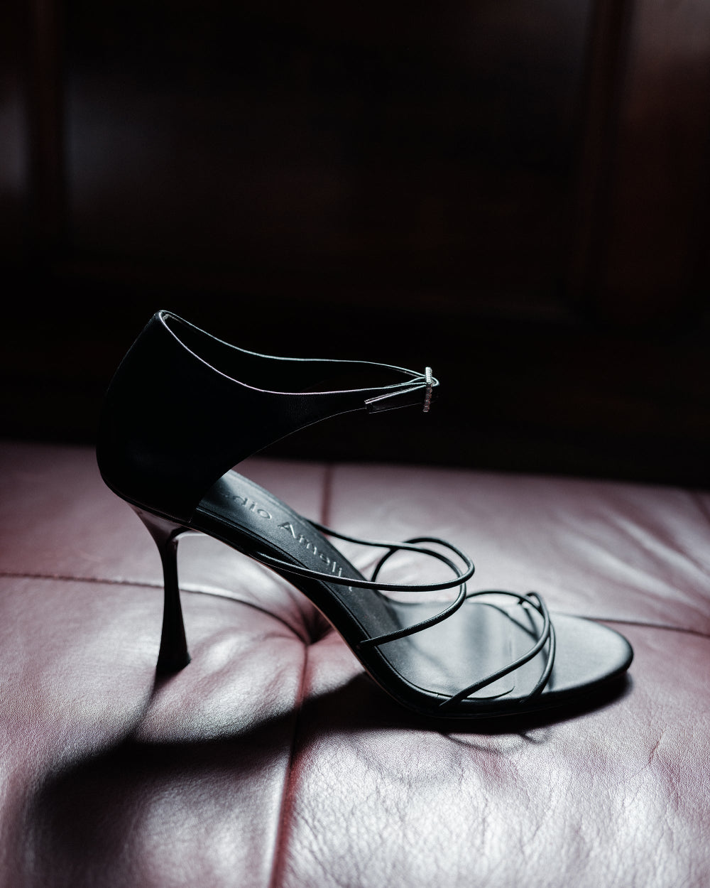 Black high-heeled sandal with thin straps on a textured surface