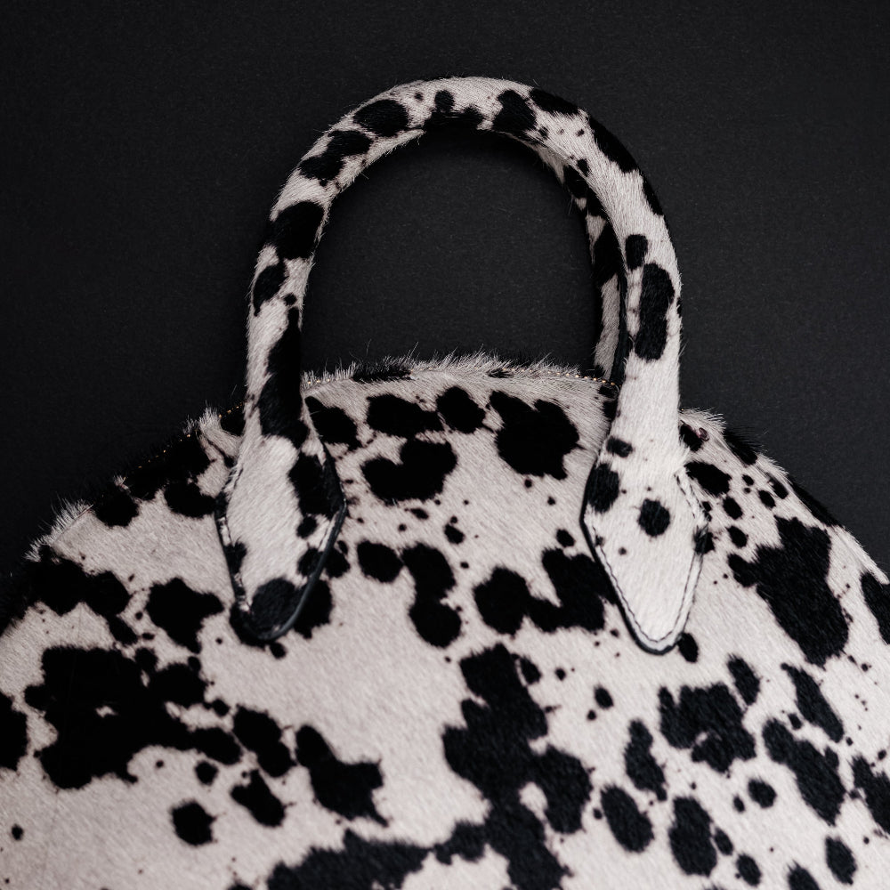 Black and white spotted handbag with a textured handle on a black background