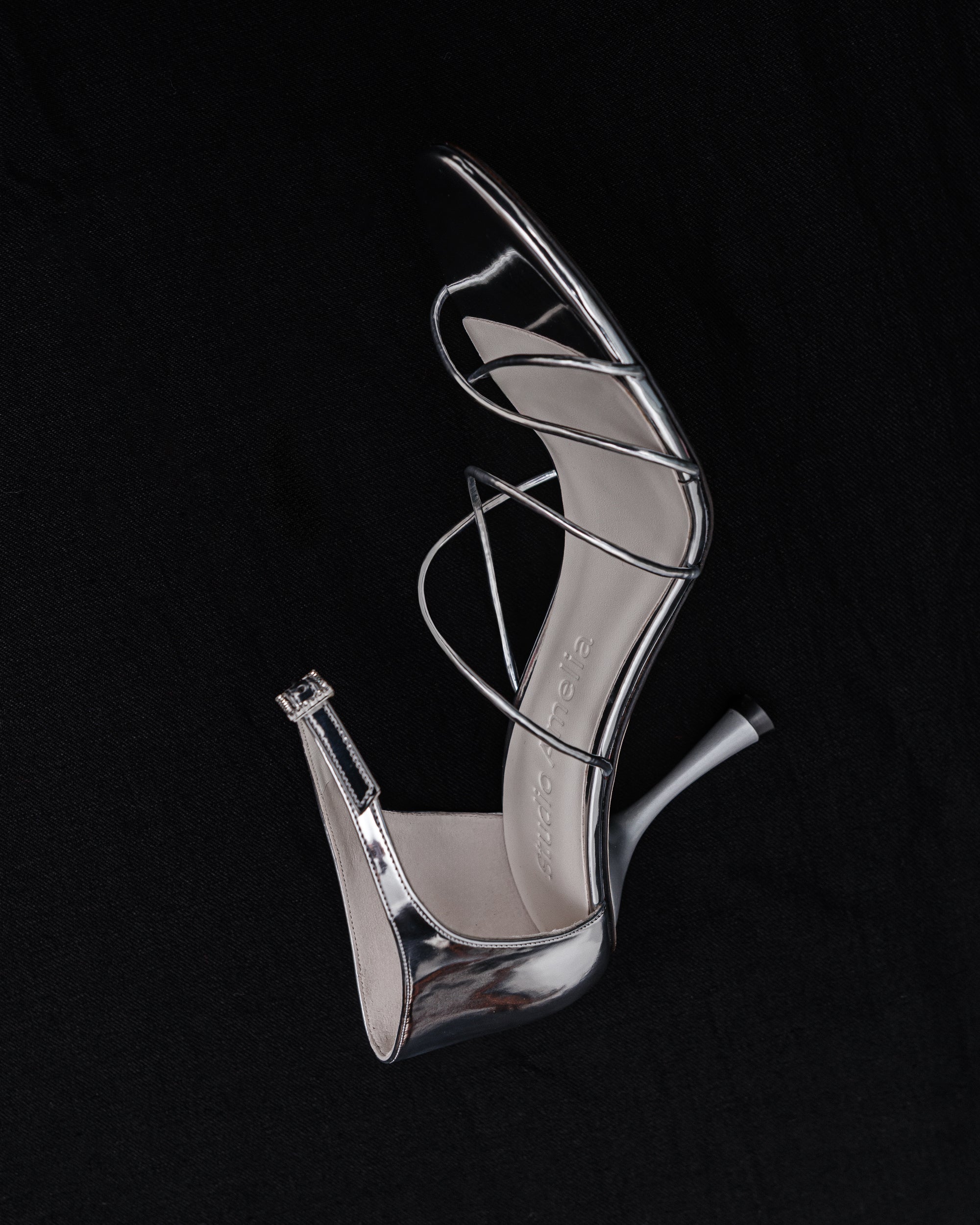 Silver high-heeled shoe with criss-cross straps on a black background