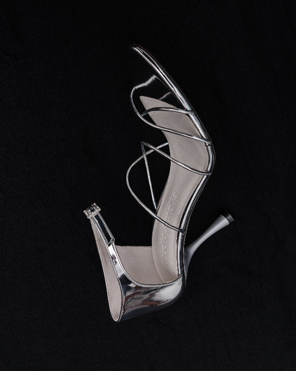 Silver high-heeled shoe with criss-cross straps on a black background